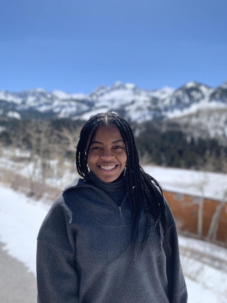 Portrait of a young woman smiling. Background includes a snow-covered mountain and blue sky. 